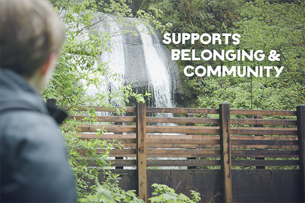 A person standing on a wooden bridge looking out at a waterfall, symbolizing connection