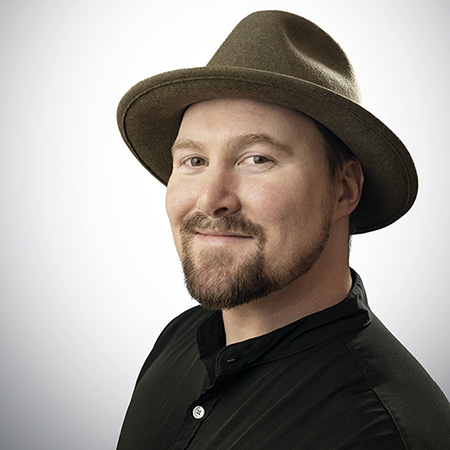 Headshot of Director Bret Malley smiling and wearing a fedora hat